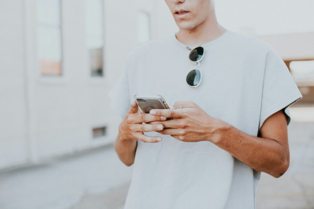 A man in white crew neck top using smartphone outdoors.