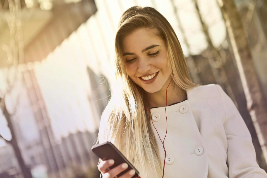 Young blonde woman holding smartphone and wearing headphones