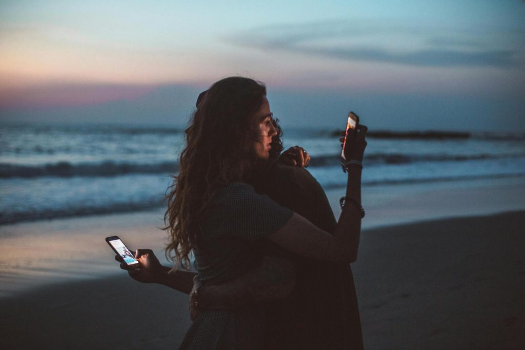 Couple hugging and using smartphone near sea on sunset.