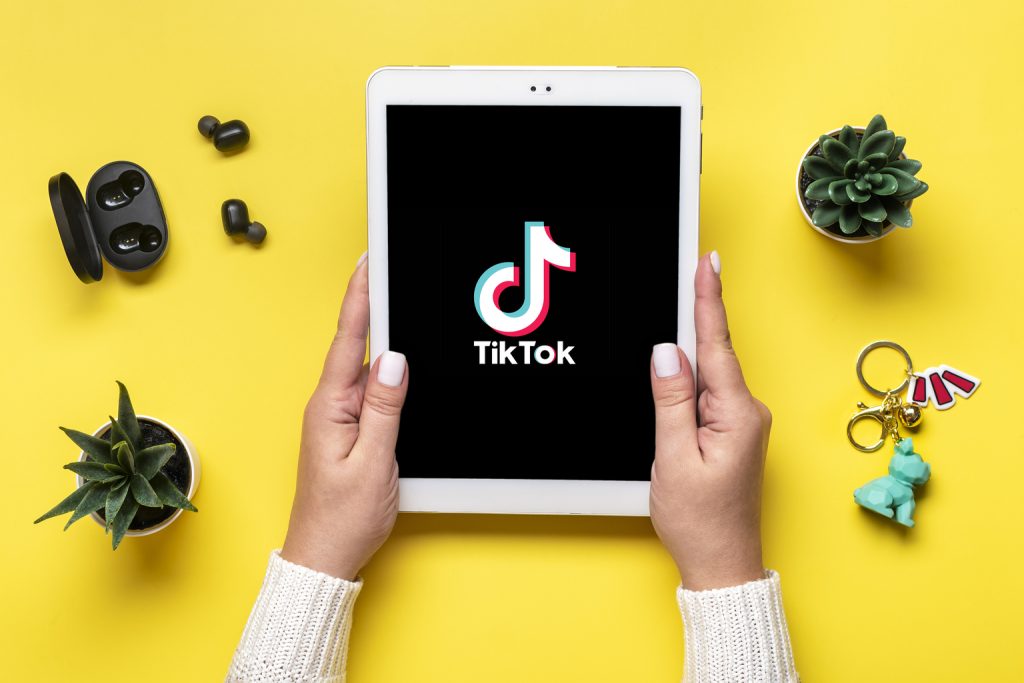 Tablet Tik Tok application icon, logo on screen and wireless headphones on colorful background Trendy social media network concept Flat lay Top view.
